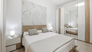 Un dormitorio moderno con una cama grande, una mesita de noche con lámpara, un espejo y un armario.