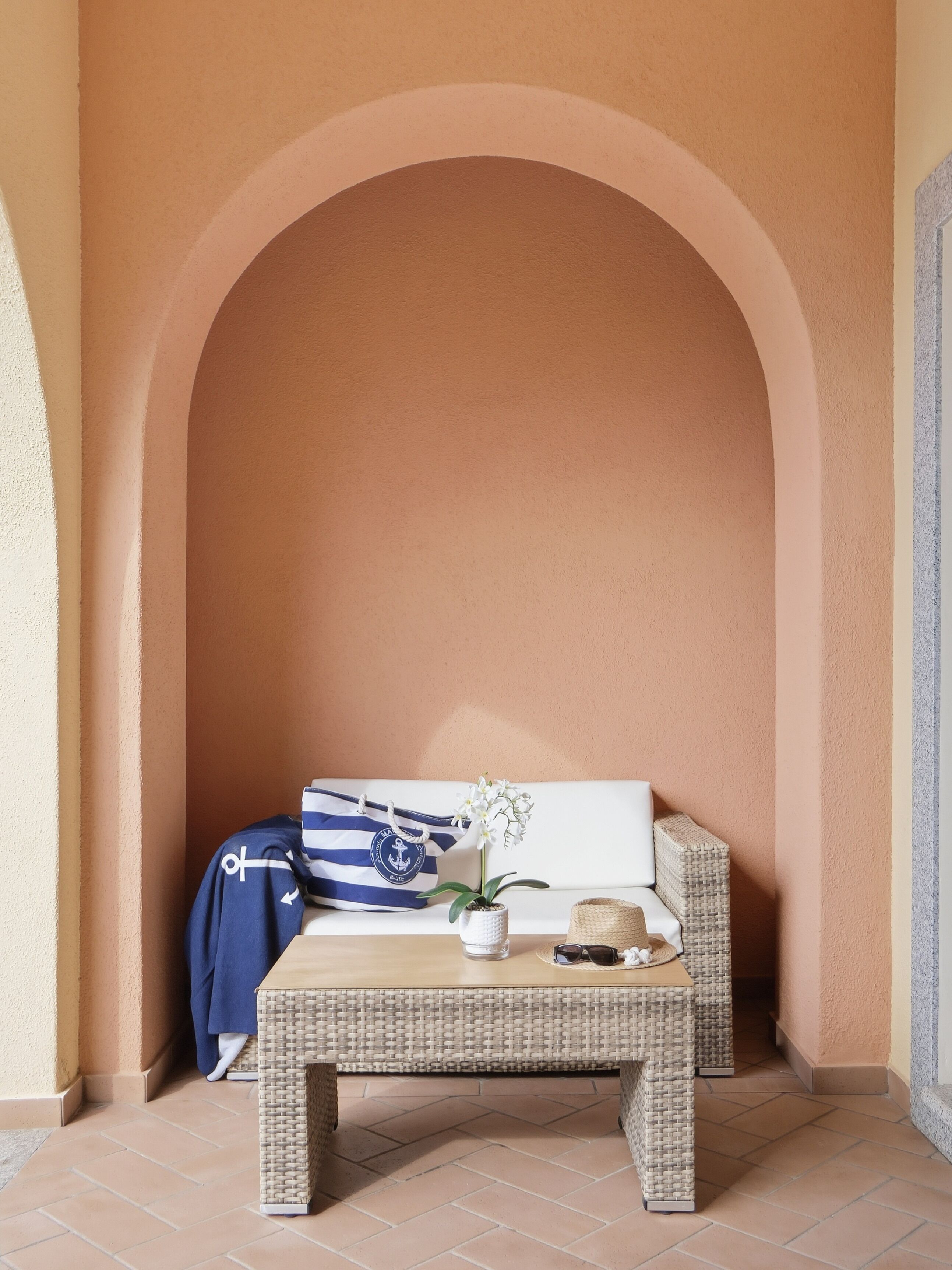 A cozy seating area with a wicker table, a white potted orchid, and a striped bag against a peach-colored wall.