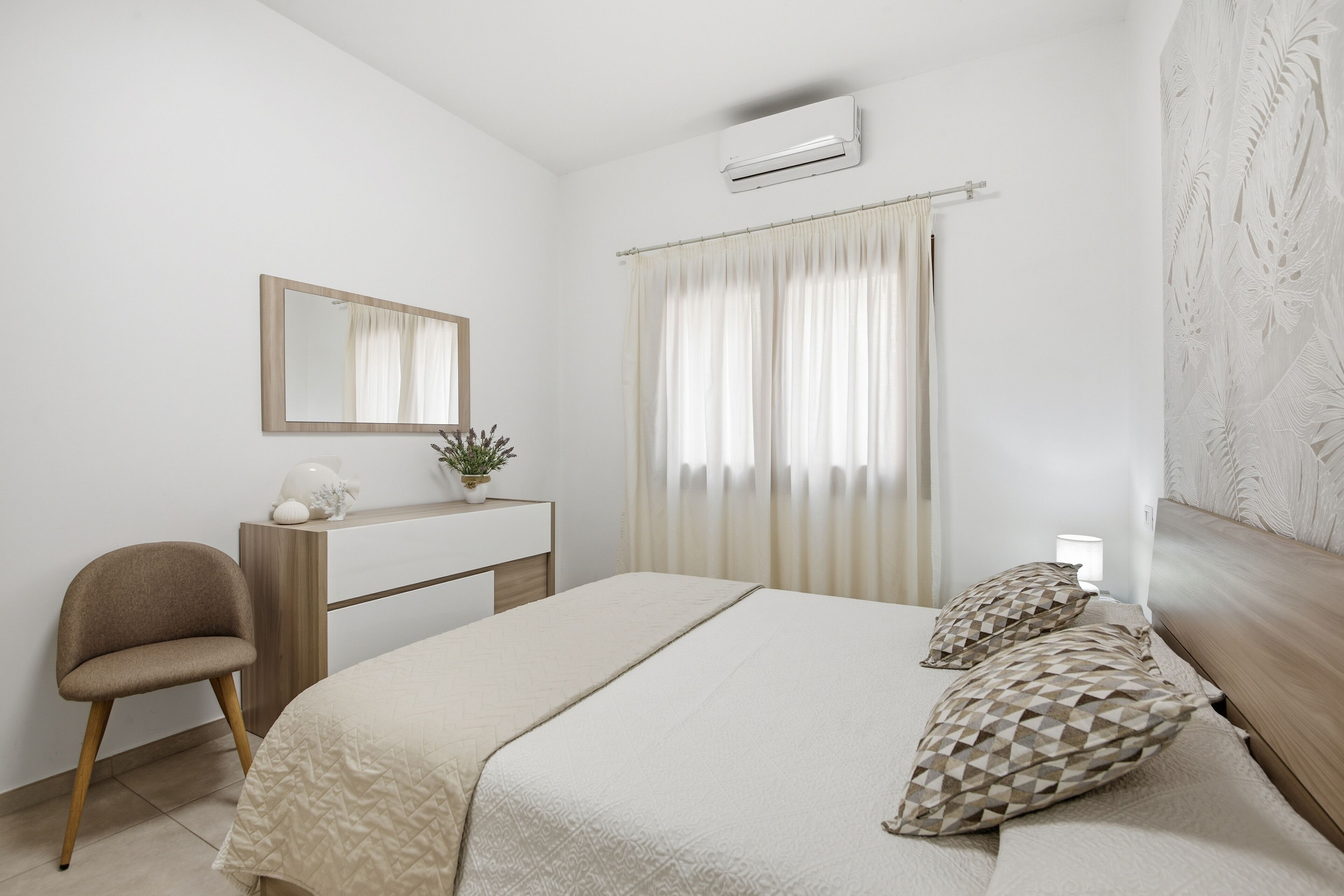 Un dormitorio con cama, una silla, un escritorio, un espejo y una ventana con cortinas.