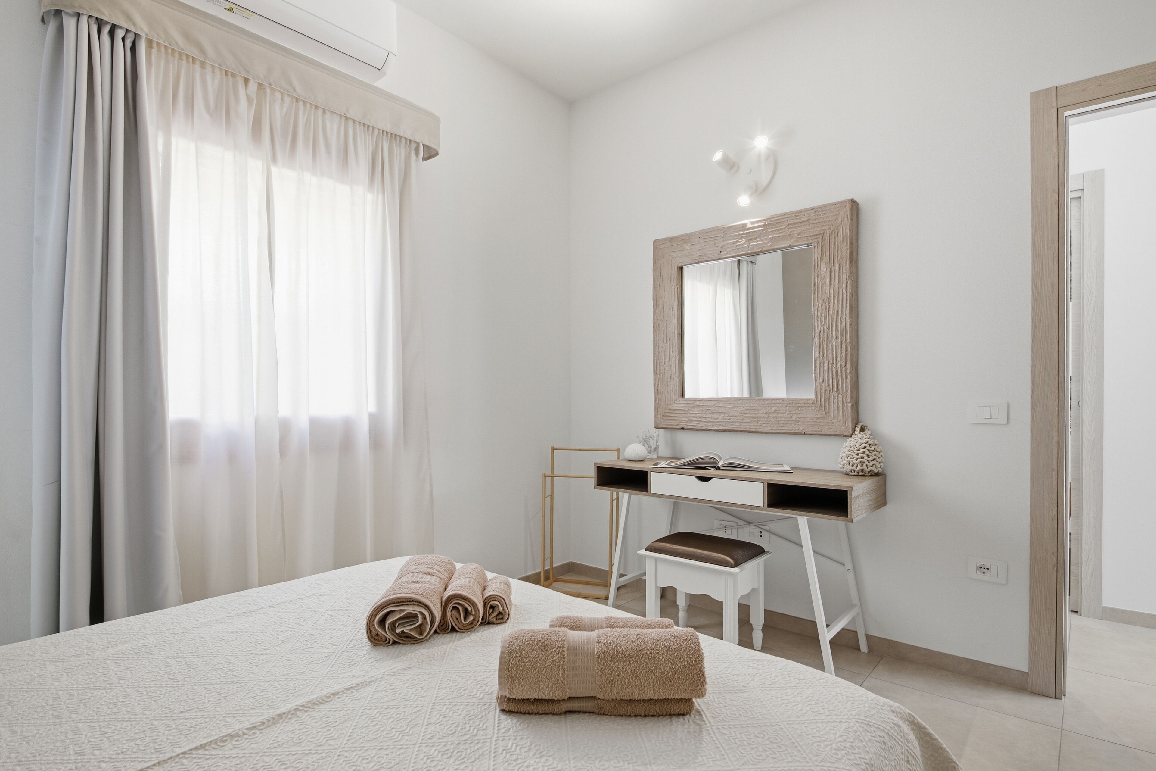 A hotel room with a bed, a desk, a chair, a mirror, and a window with curtains.
