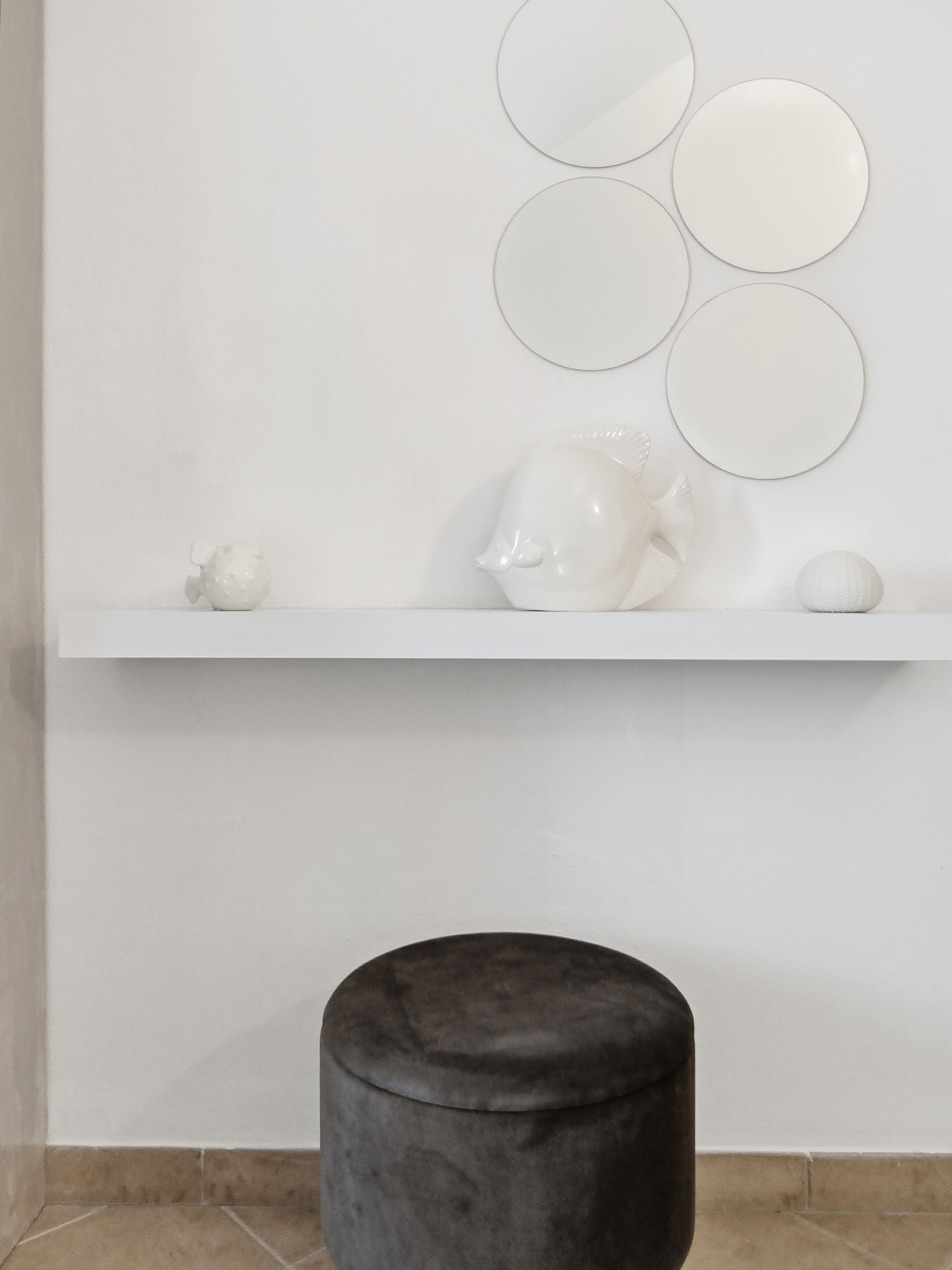 A white shelf with decorative items, a round stool, and wall-mounted mirrors.