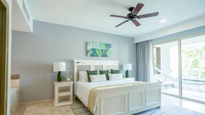 Une chambre à coucher avec un lit, des tables de chevet, un ventilateur de plafond et une grande fenêtre.