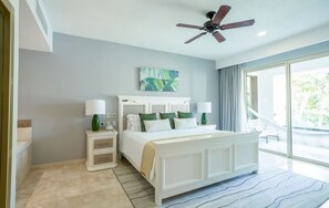 Une chambre à coucher avec un lit, des tables de chevet, un ventilateur de plafond et une grande fenêtre.