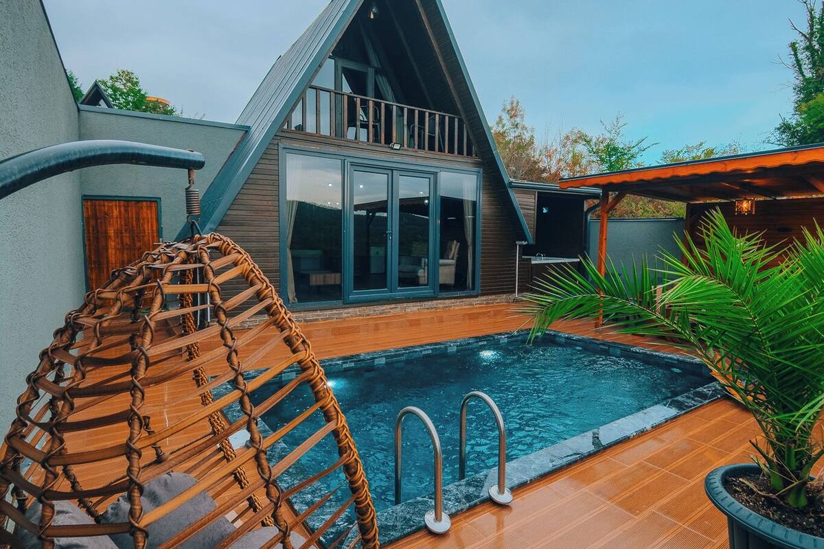 Une maison moderne avec une piscine, un fauteuil suspendu et une terrasse en bois.