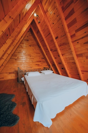 Una habitación con techo inclinado, vigas de madera, cama con ropa blanca y una alfombra de piel.