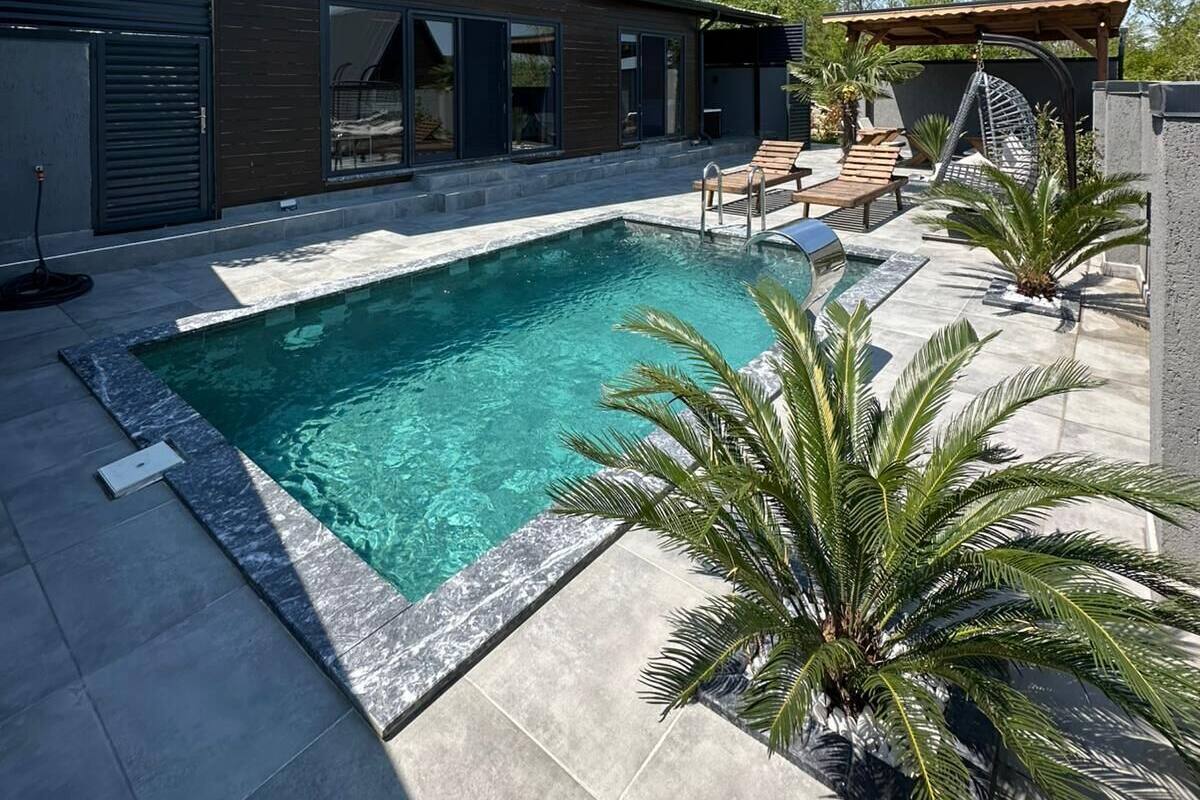 Une maison moderne dotée d’une piscine, d’une terrasse en bois et d’un espace extérieur aménagé et couvert.
