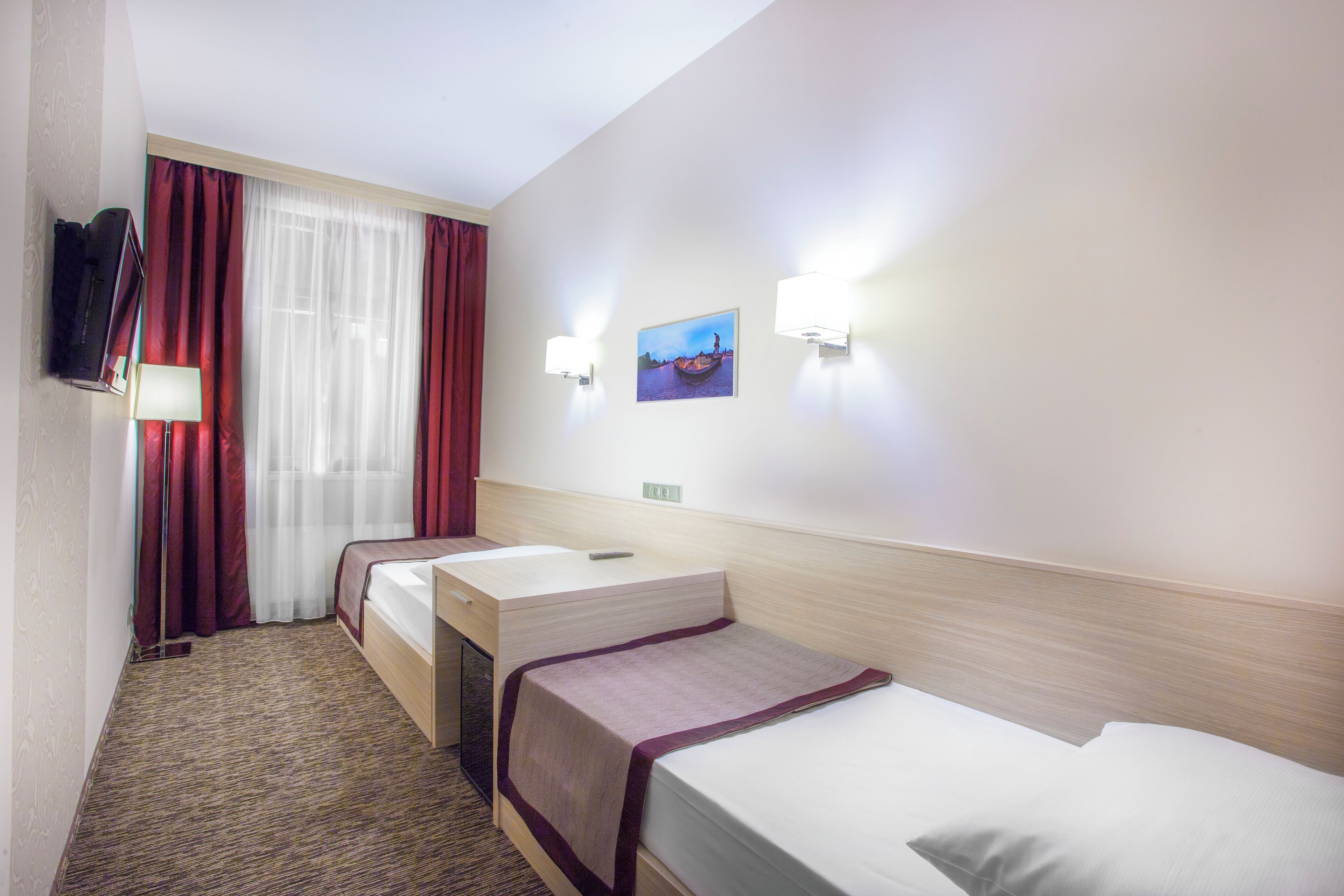 A hotel room with two single beds, a desk, a chair, a TV, and a painting on the wall.