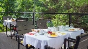 Un espace de restauration en plein air, avec des tables dressées pour le petit-déjeuner, entouré d’une végétation luxuriante.