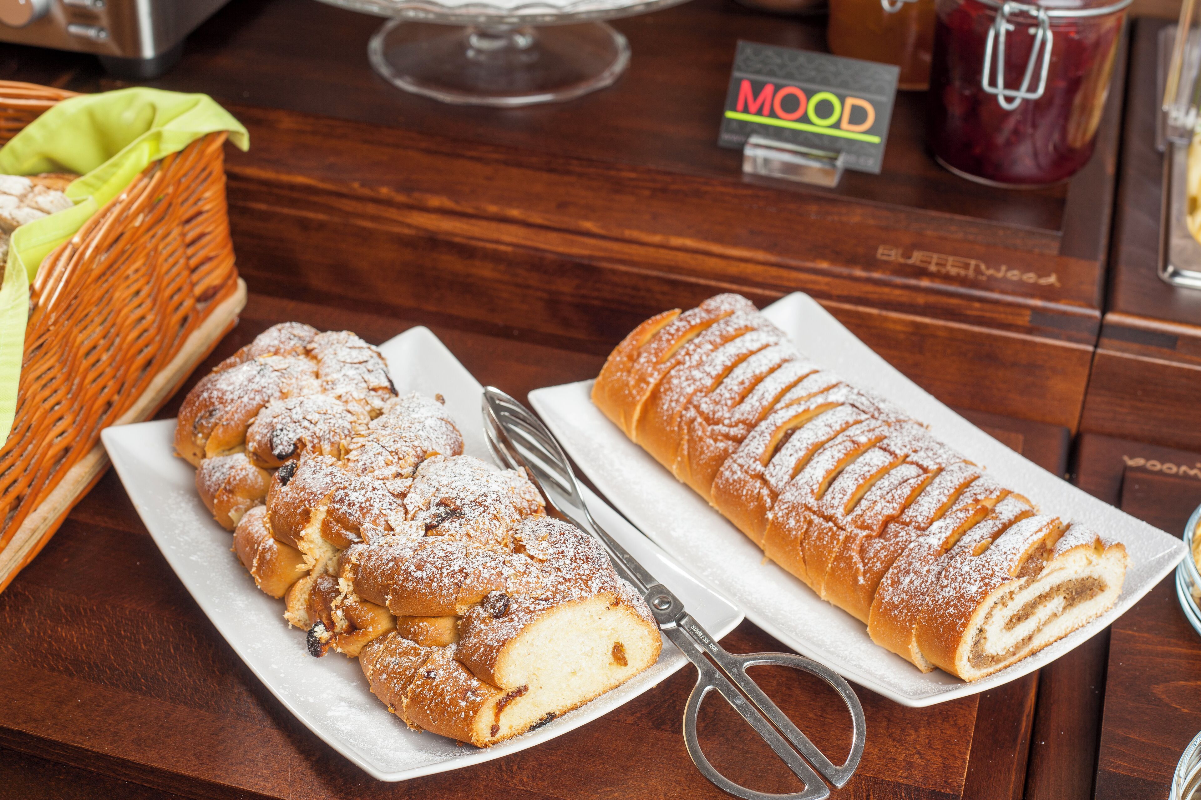 A wooden table with a white plate holding a sliced pastry and a loaf of bread.