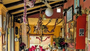 A long dining table set with red napkins, clear glasses, and cutlery, decorated with hanging ornaments and a chandelier.