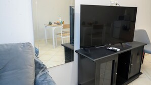 Un soggiorno moderno con una TV a schermo piatto su un mobile nero, un divano grigio e un tavolino con una sedia sullo sfondo.