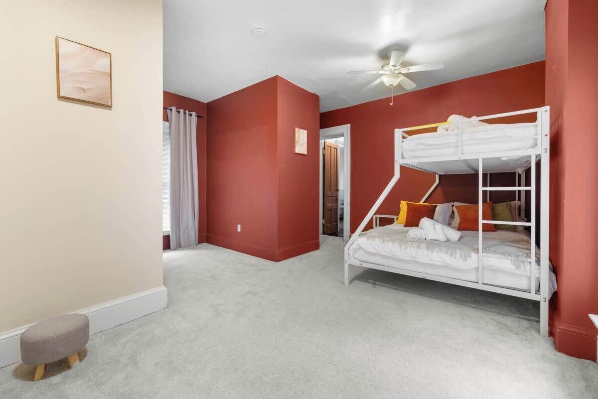 A room with a bunk bed, a ceiling fan, and a door leading to another room.