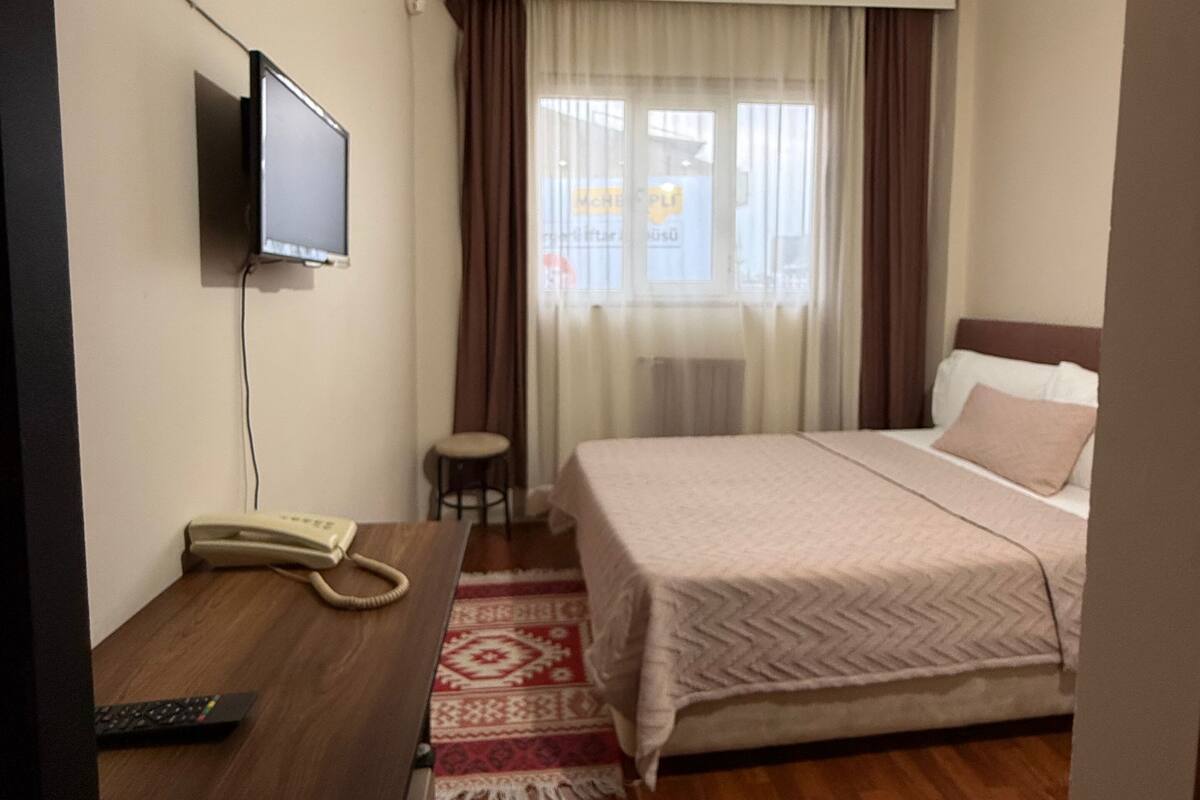 A hotel room with a bed, a desk with a telephone, a television mounted on the wall, and a window with curtains.