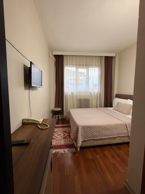 A hotel room with a bed, a desk with a telephone, a television mounted on the wall, and a window with curtains.