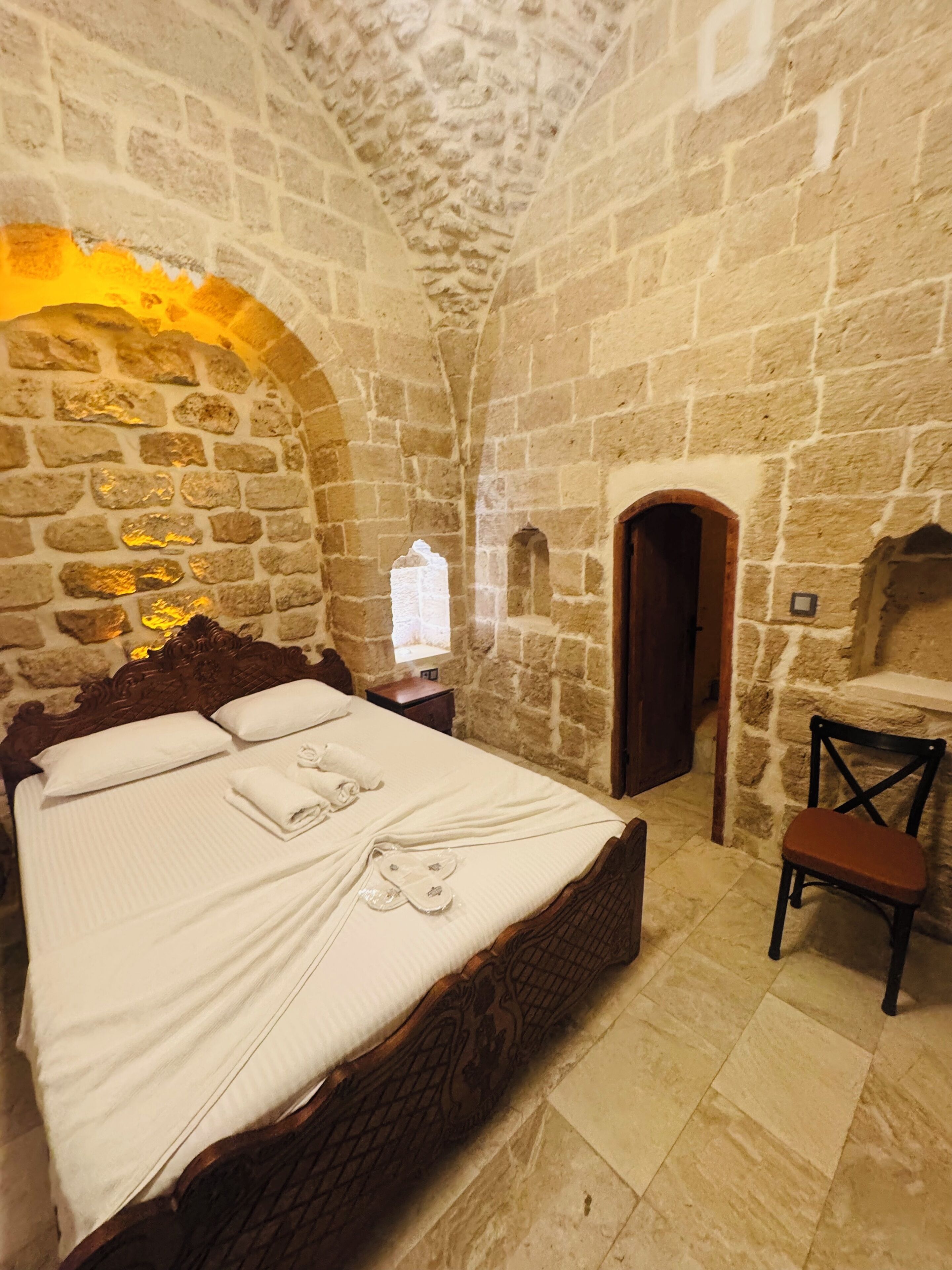 A stone-walled room with a bed, a chair, and a small table.