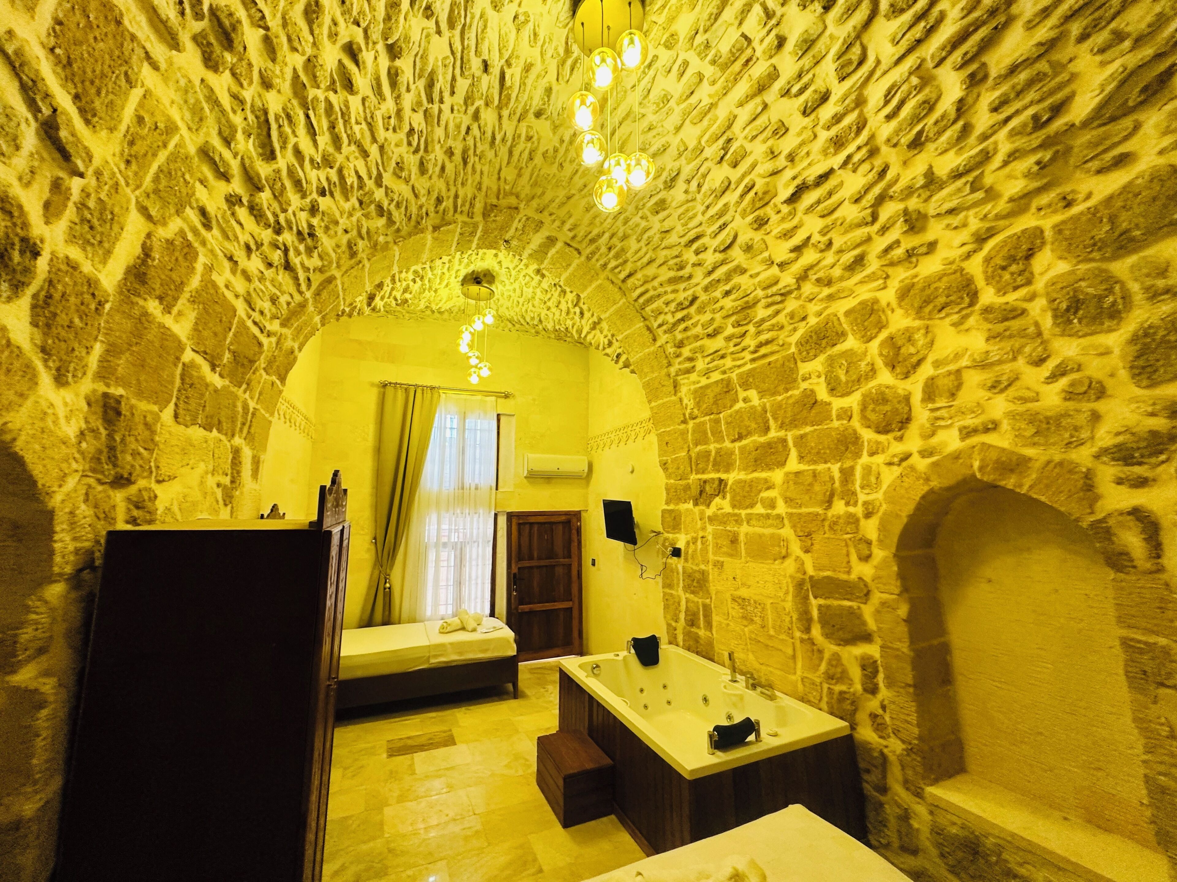 Ein Zimmer mit Steinwänden, einem Bett, einem kleinen Tisch und einer Badewanne.