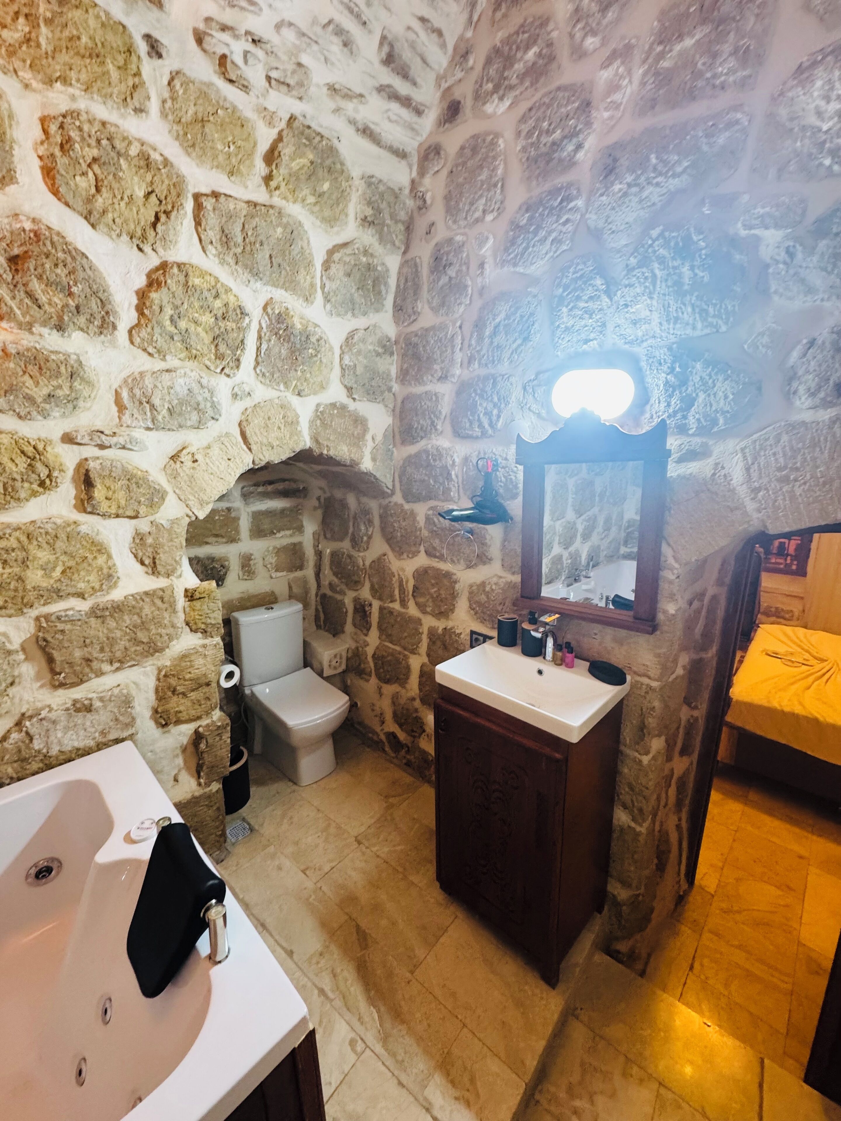 Baño con paredes de piedra, lavamanos, inodoro y espejo.