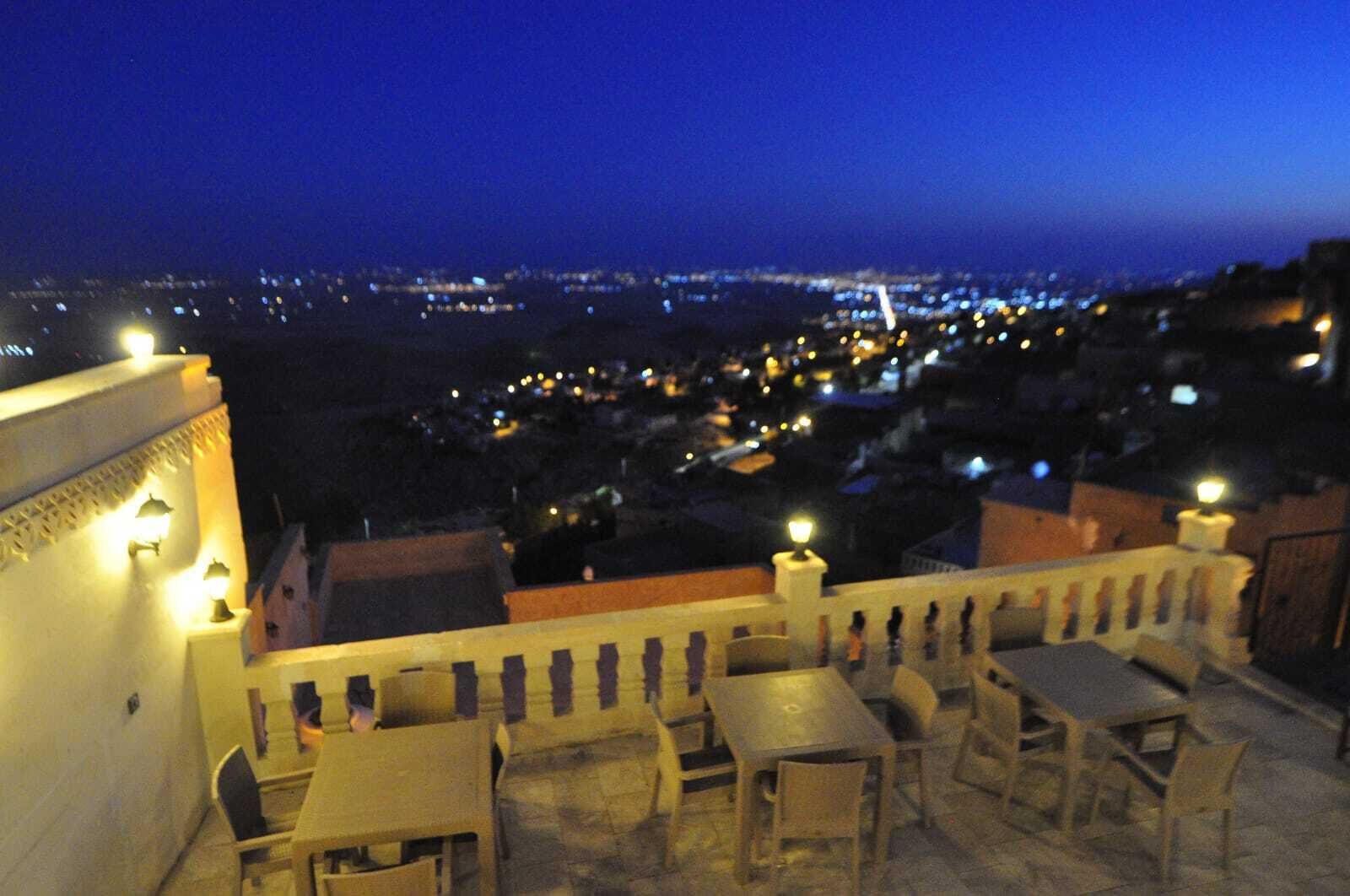 A terrace with tables and chairs, overlooking a cityscape at night.