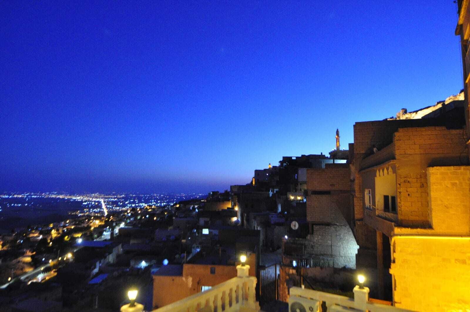 A nighttime view of a densely built urban area with illuminated buildings and a distant cityscape.