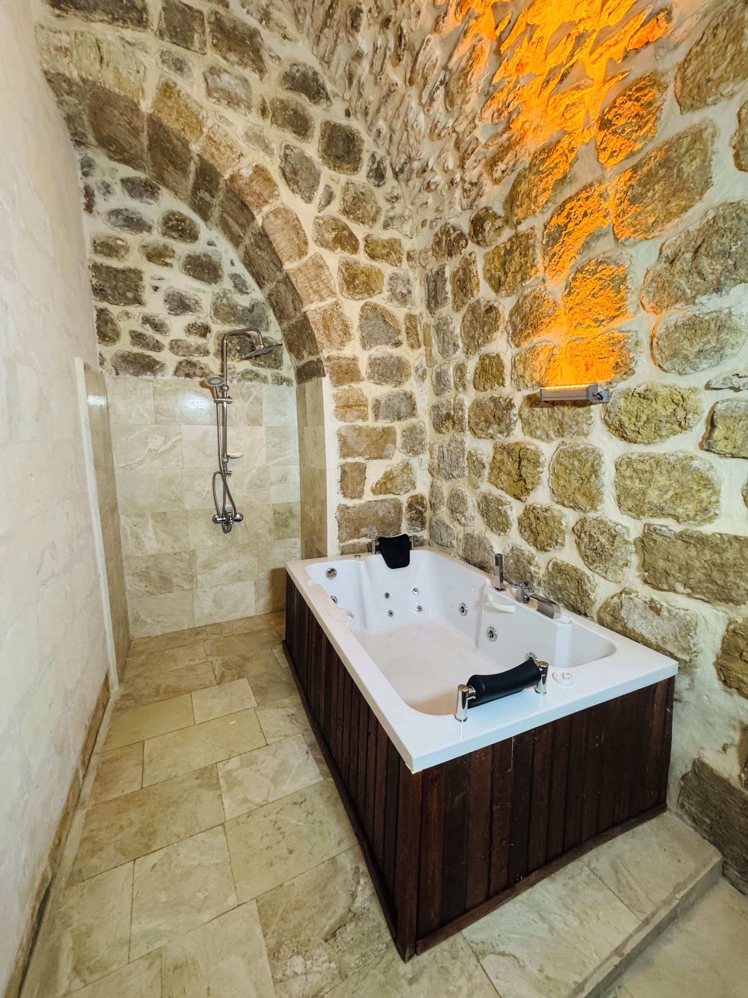 A stone-walled bathroom with a freestanding bathtub and a shower area.