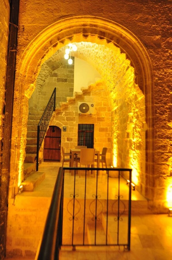 An arched stone corridor with a staircase leading to a room with a wooden door and a window. - Kasr-i Ahenk Konaği (Mardin)