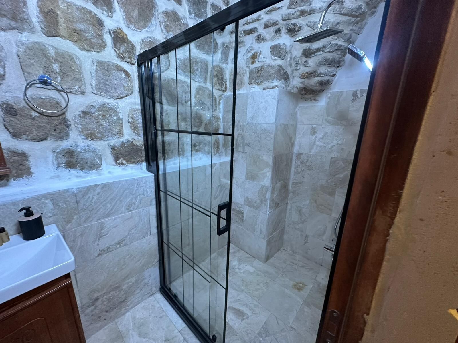 Une douche en verre avec des murs en pierre et une baignoire visible sur la gauche.