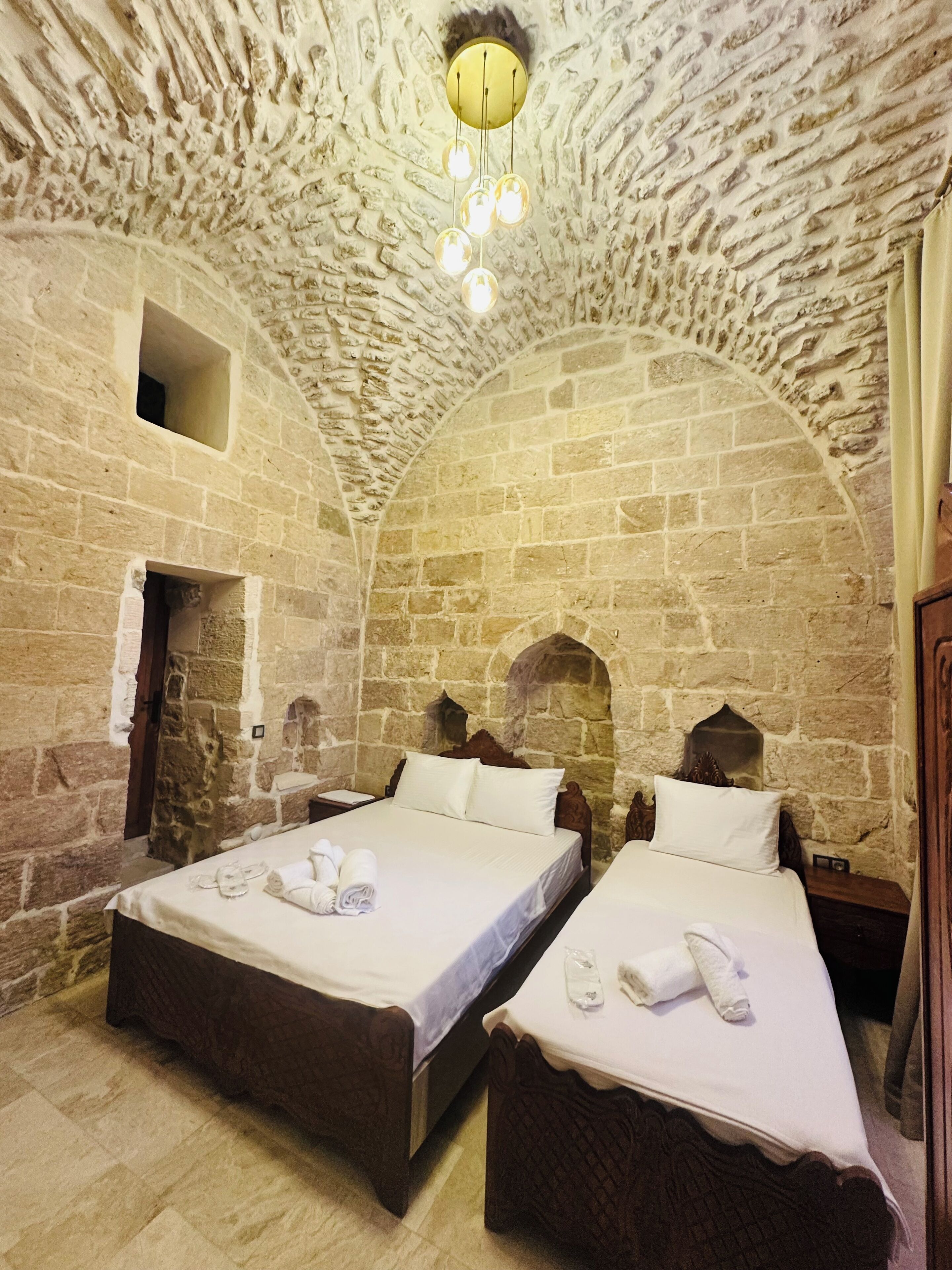 A room with two beds, stone walls, and a unique arched ceiling.