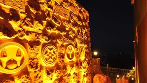 Een stenen muur met verlichte symbolen, een lantaarnpaal en een uitzicht op een stadsbeeld 's nachts.