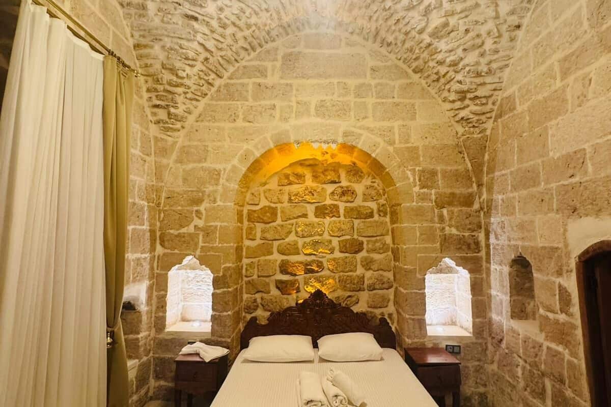 Ein Zimmer mit Steinwänden, einem Bett, einer Chandelier und einem Fenster.
