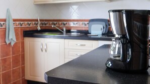Een keuken met een koffiezetapparaat op het aanrecht, kastjes en een betegelde achterwand.