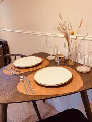 A dining table set with plates, cutlery, and wine glasses, accompanied by a vase with dried plants. - The Hayloft at Brylach Steading, Speyside. (Aberlour)