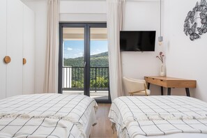 A hotel room with two beds, a desk, a chair, a TV, and a balcony with a view of the hills. - Relaxed Family Villa With Private Pool (Omis)