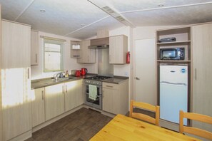 A compact kitchen with a stove, oven, sink, and a microwave on a shelf.