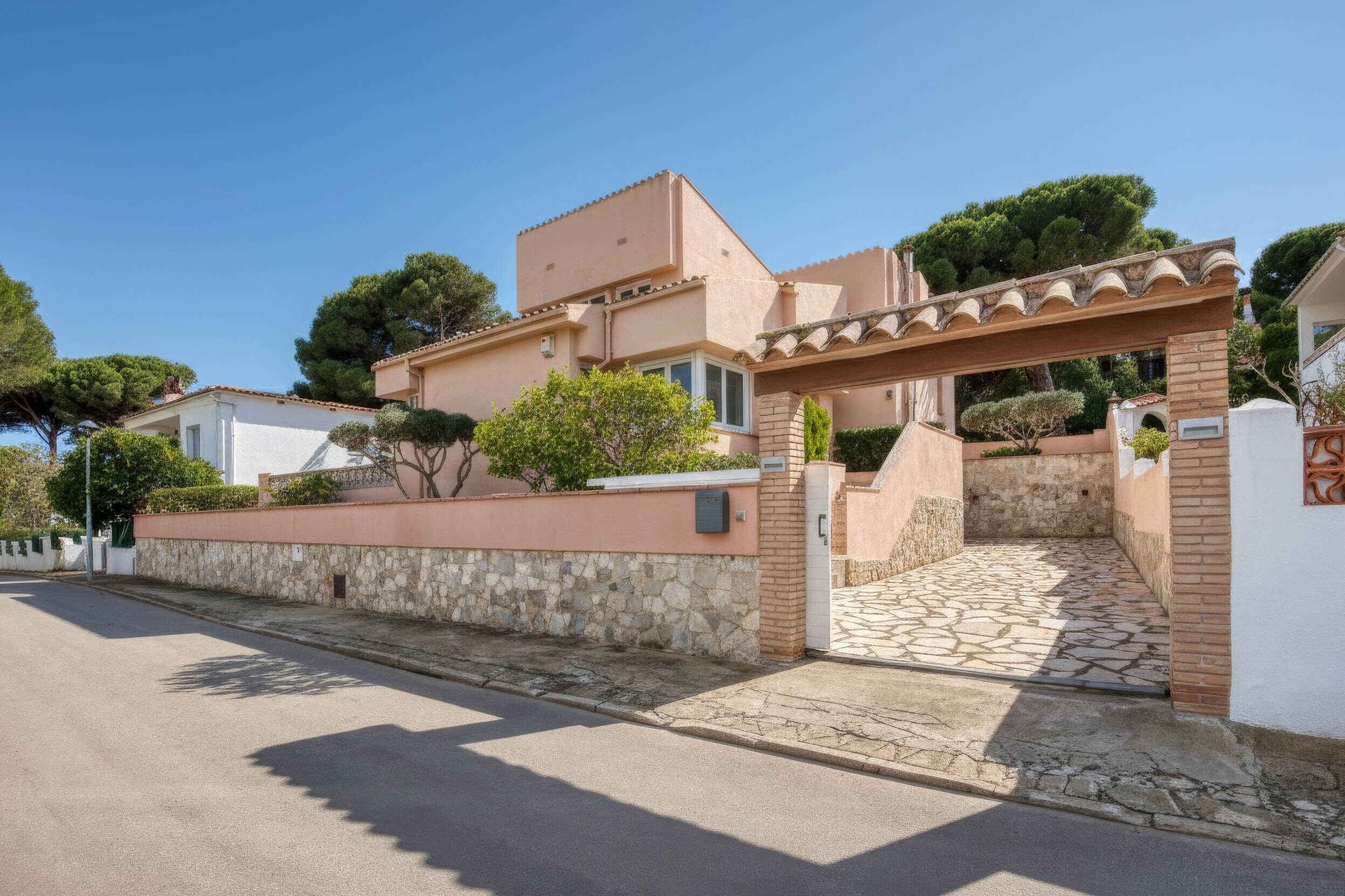 Um imóvel residencial com parede de pedra, entrada pavimentada e céu limpo.