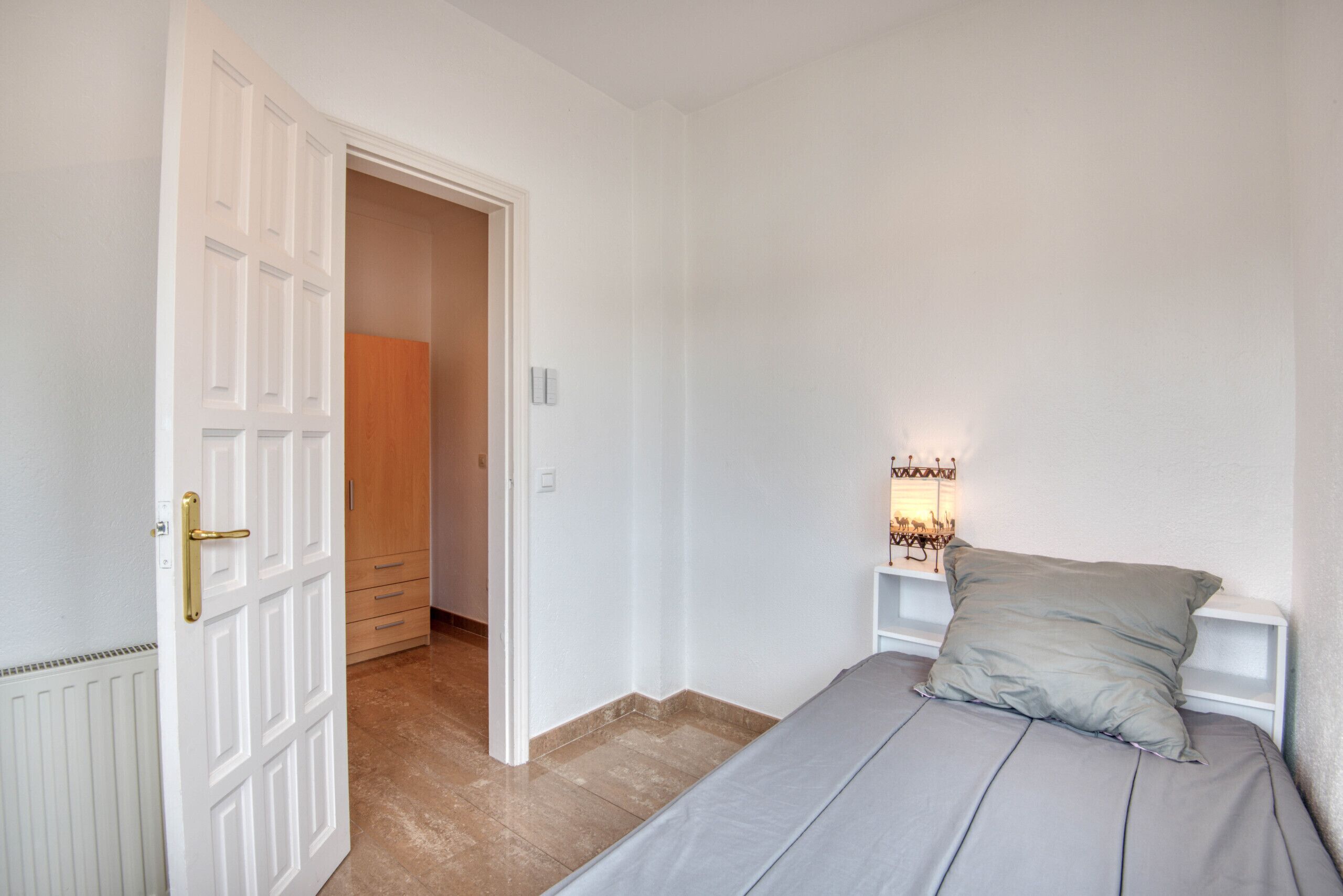 A bedroom with a bed, a nightstand, a lamp, and a door leading to another room.
