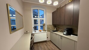 Una cocina moderna con ventana, armarios blancos, un radiador y una cafetera.