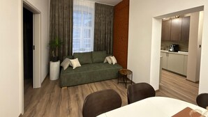 Un apartamento moderno con un sofá verde, una mesita redonda y un comedor.