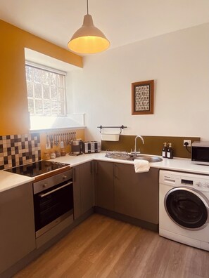 A modern kitchen with a built-in oven, a microwave, a sink, and a washing machine. - The Bothy at Brylach Steading, Speyside (Aberlour)