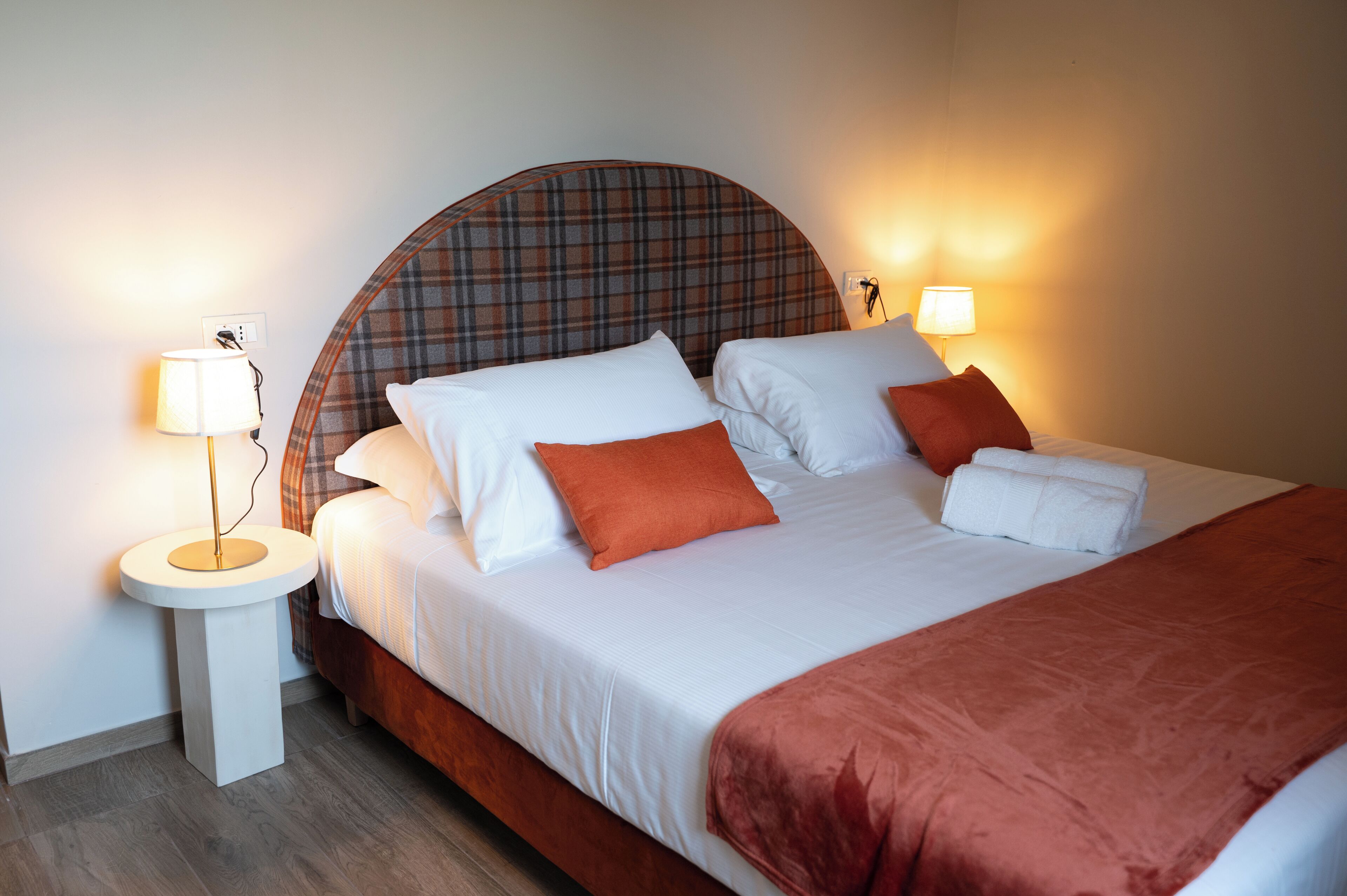 A neatly made bed with white linens and a plaid headboard, accompanied by two bedside lamps and a round nightstand.