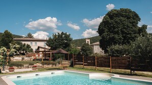Une piscine rectangulaire à l’eau d’un bleu limpide, entourée d’une clôture en bois et d’un mur de pierre.