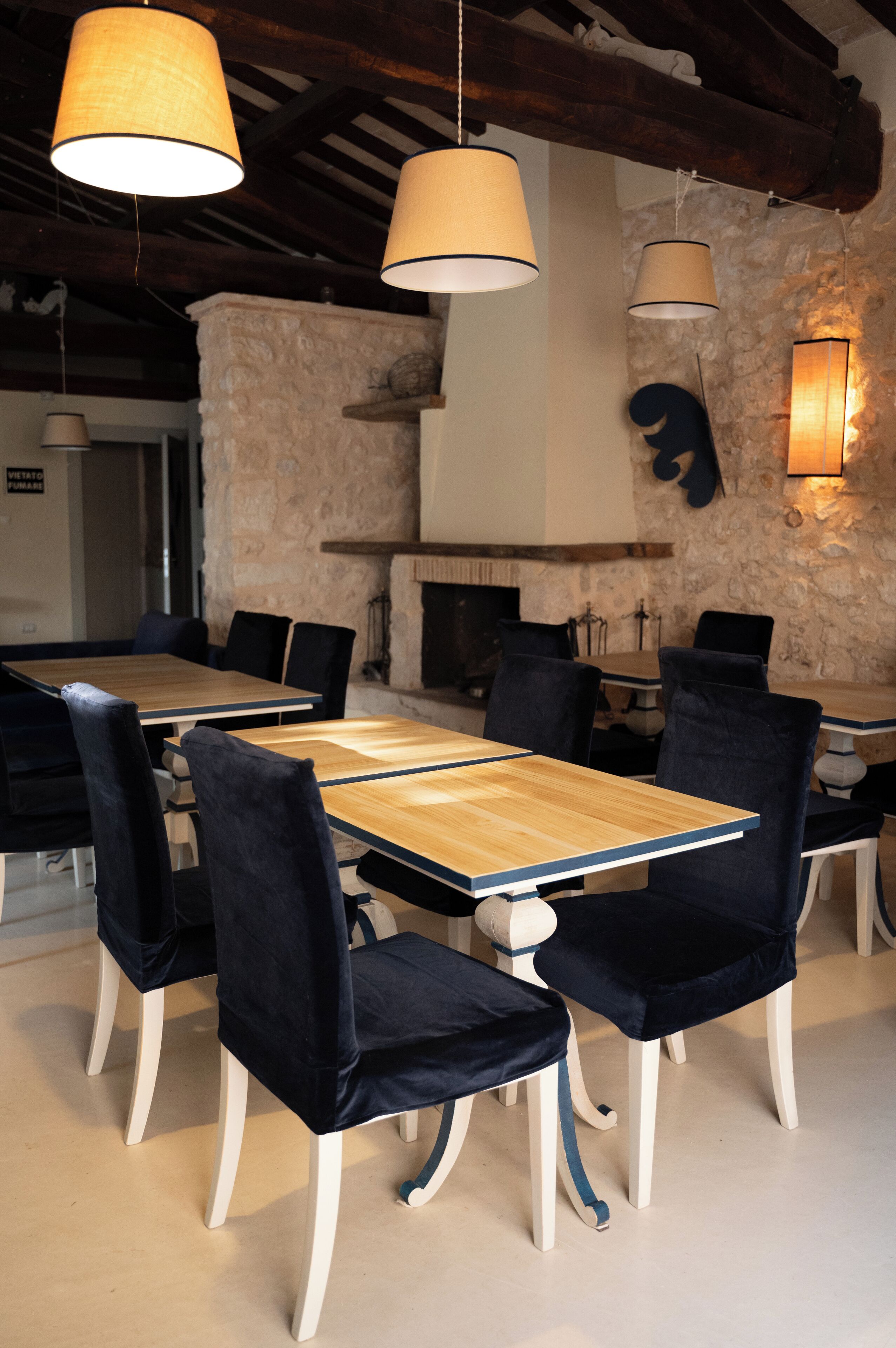 Un comedor con mesas de madera, sillas de terciopelo negro, paredes de piedra y lámparas colgantes.