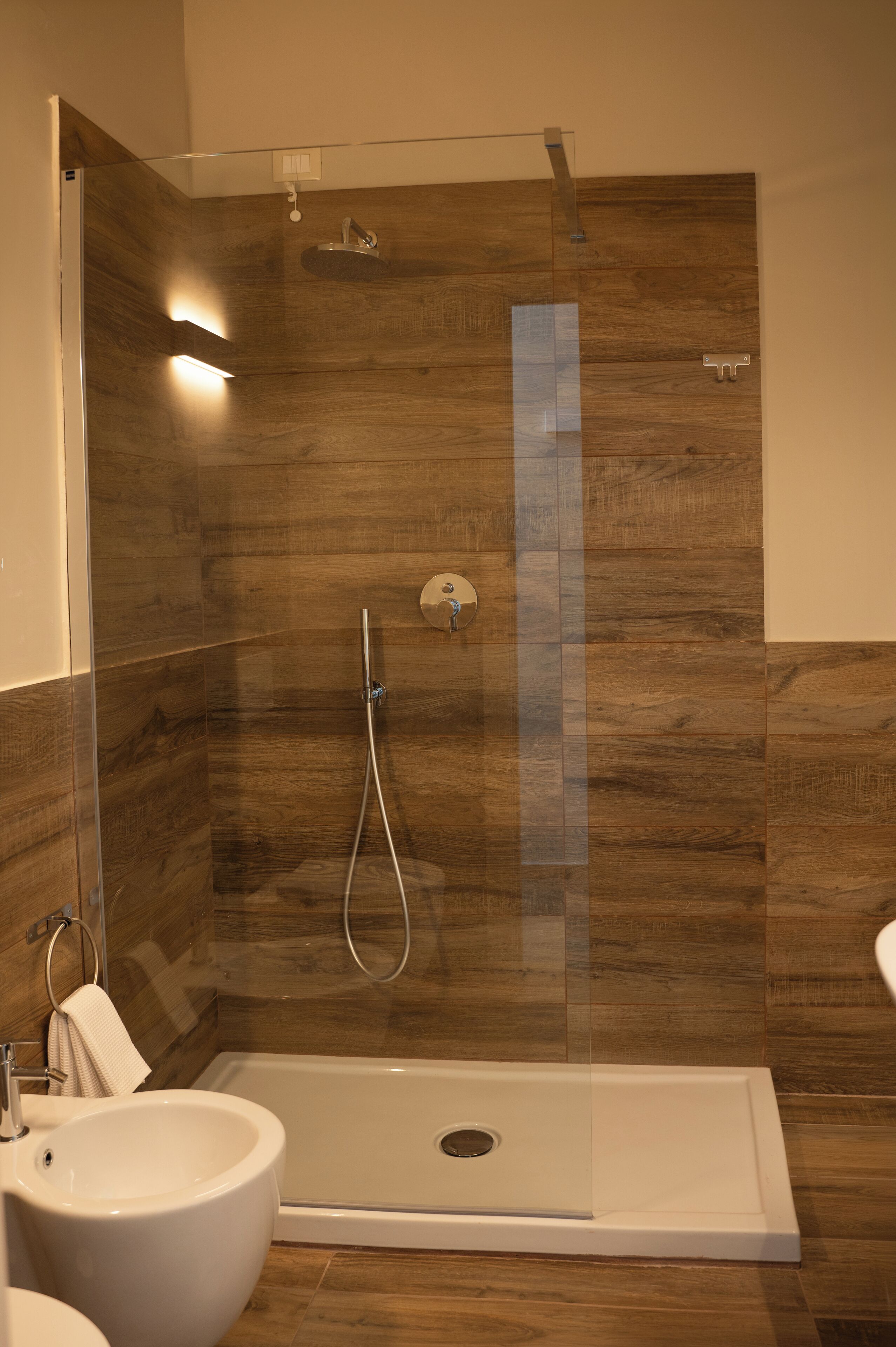 A modern bathroom with a glass-enclosed shower, a white sink, and a wooden floor.