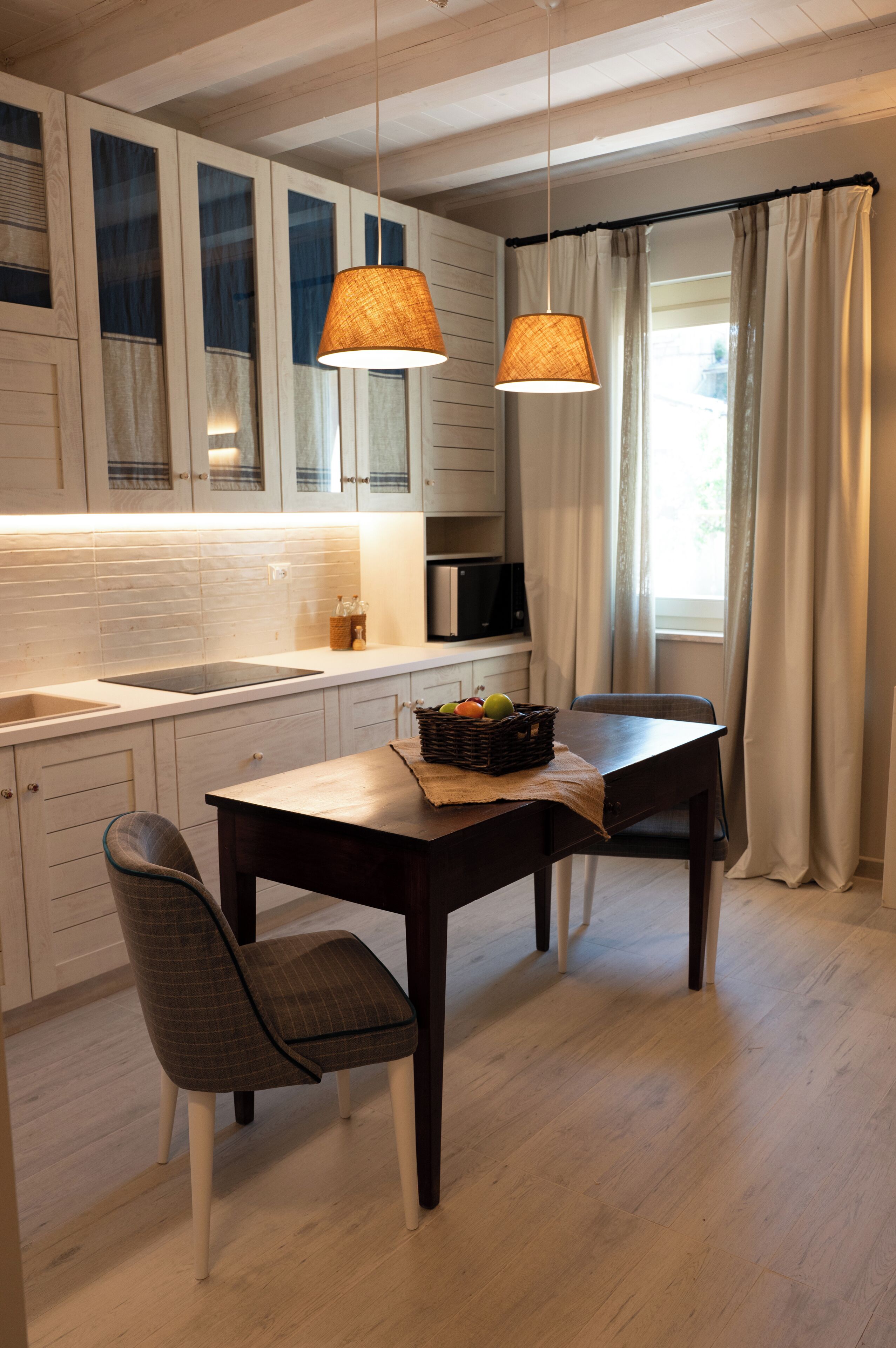 Una cocina moderna con armarios blancos, una mesa de comedor de madera, dos sillas y una lámpara colgante.