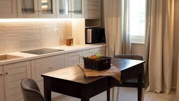 Una cocina moderna con armarios blancos, una mesa de comedor de madera, dos sillas y una lámpara colgante.