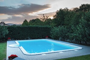 Ein rechteckiger Pool mit Fliesen umgeben von dichtem Grün und Bäumen.