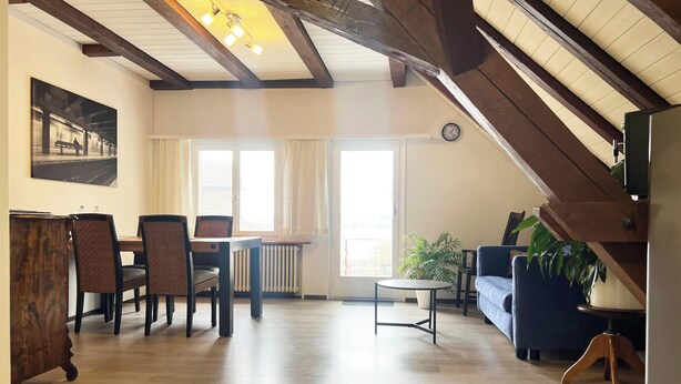 A spacious living area with wooden beams, a dining table with chairs, a sofa, and a potted plant. - Lake View Apartment, 2 min from Lake Constance. Balcony. Pets are welcome! (Ermatingen)