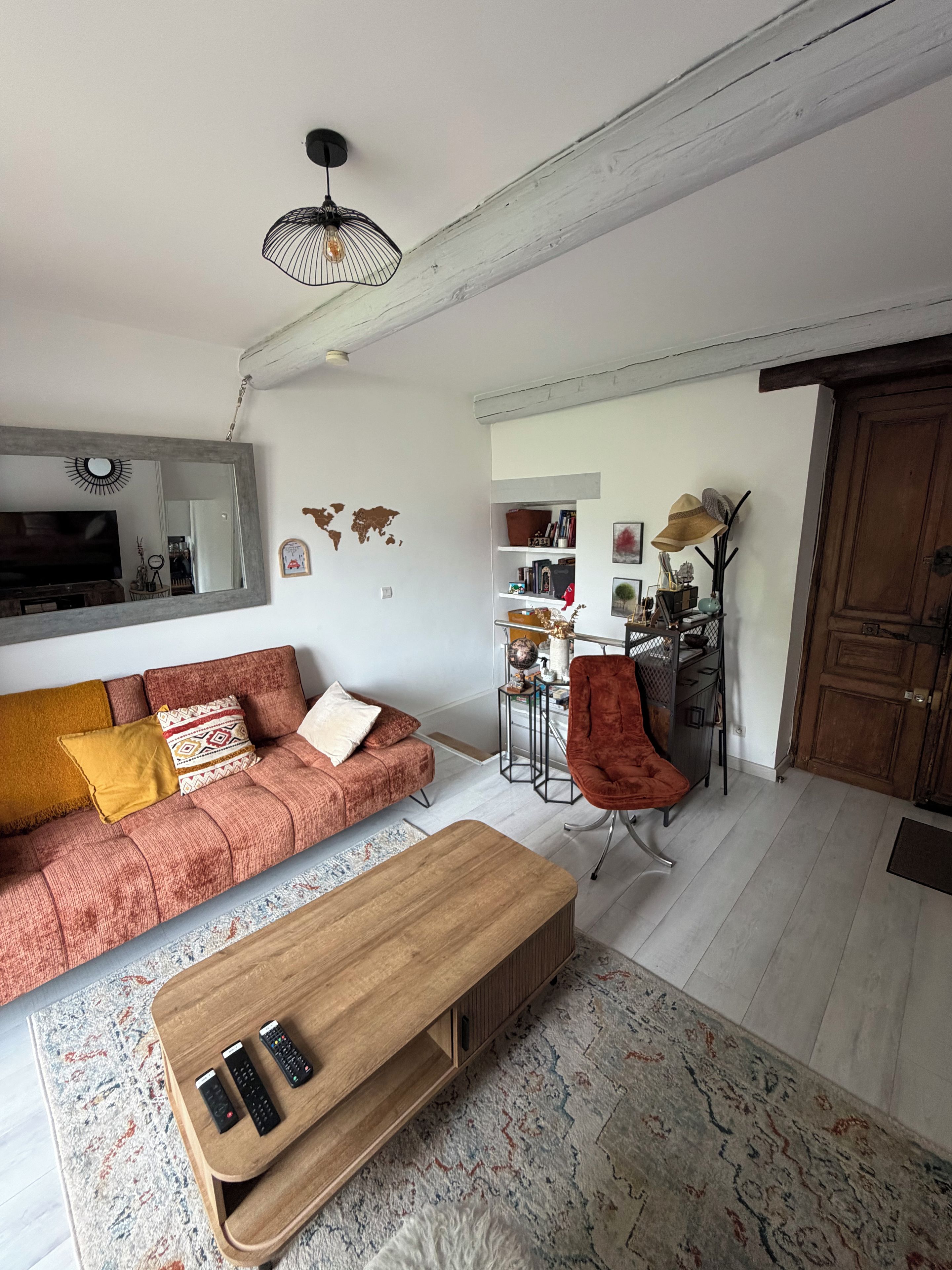 Un salón con sofá, una mesa de centro y televisor. Hay un mapa mundial en la pared y una puerta a la derecha.