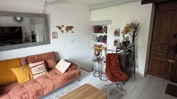 Un salón con sofá, una mesa de centro y televisor. Hay un mapa mundial en la pared y una puerta a la derecha.