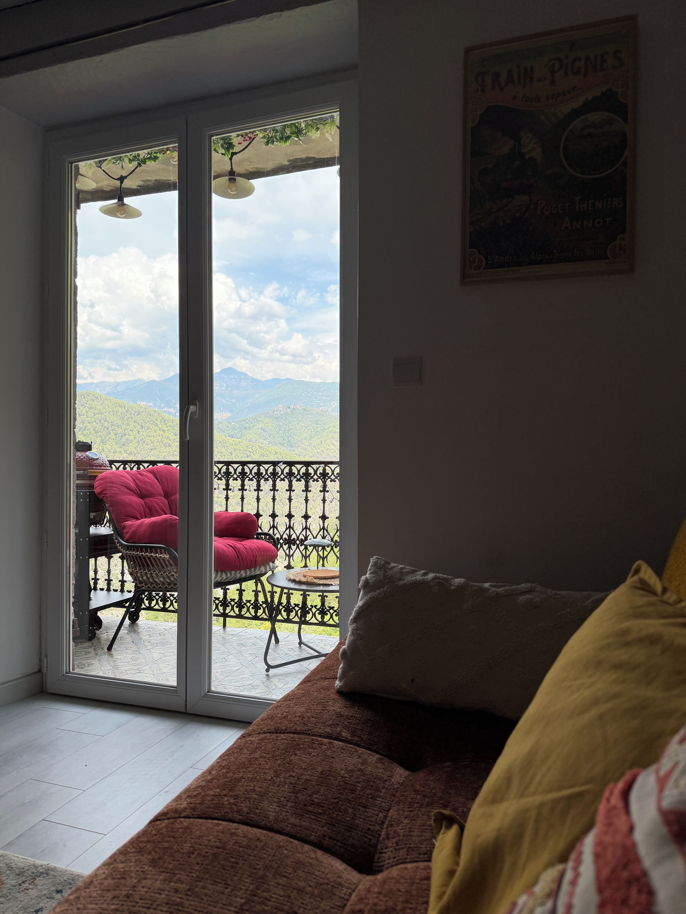 Een kamer met een schuifdeur die uitkomt op een terras buiten, met een rode stoel en een tafel.