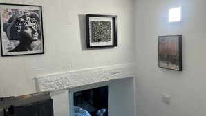 Ein Zimmer mit weißer Wand, einem gerahmten Kunstwerk, einem kleinen Fenster und einer teilweise sichtbaren Tür.
